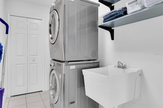clothes washing area with stacked washer / drying machine, light tile patterned flooring, a sink, and laundry area