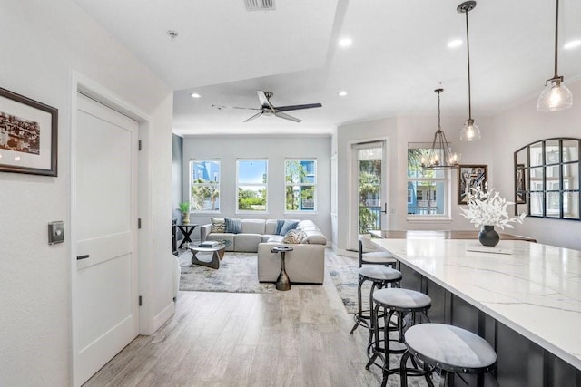 interior space featuring recessed lighting, light wood-style flooring, light stone counters, ceiling fan with notable chandelier, and a kitchen bar