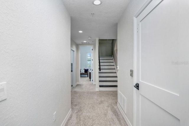 hallway featuring stairway, visible vents, baseboards, recessed lighting, and light carpet