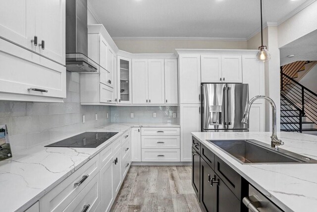 kitchen with wall chimney range hood, crown molding, white cabinets, a sink, and stainless steel appliances