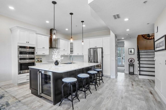 kitchen with a sink, appliances with stainless steel finishes, visible vents, wall chimney exhaust hood, and wine cooler