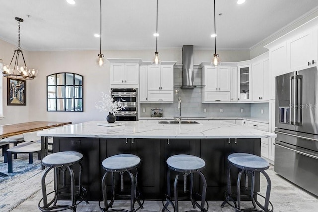 kitchen with stainless steel appliances, wall chimney range hood, a sink, white cabinetry, and crown molding