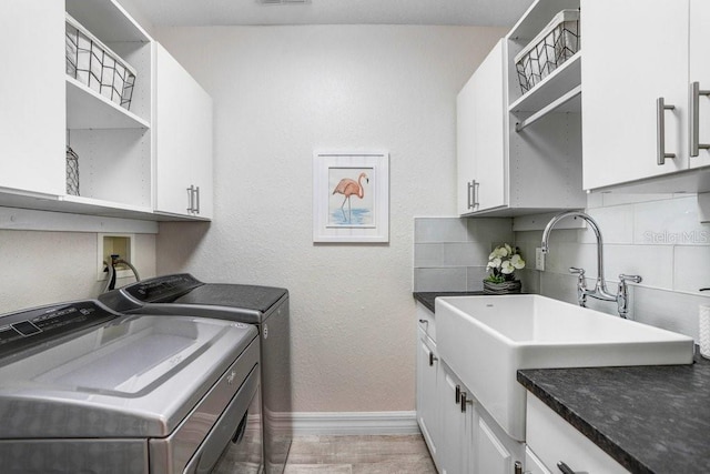 laundry area featuring separate washer and dryer, cabinet space, a sink, baseboards, and visible vents