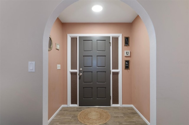 doorway featuring arched walkways, light wood-style flooring, and baseboards