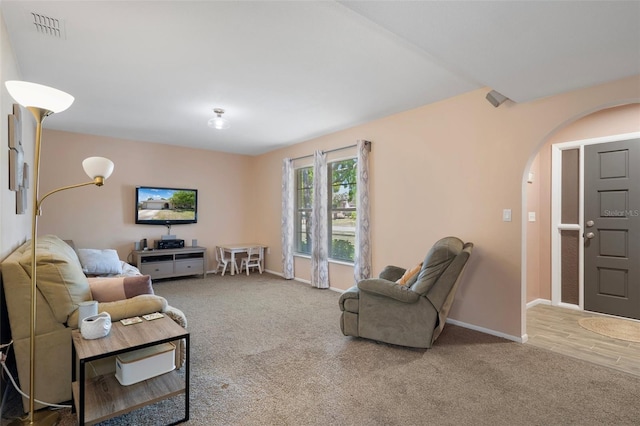 living area with arched walkways, carpet flooring, visible vents, and baseboards