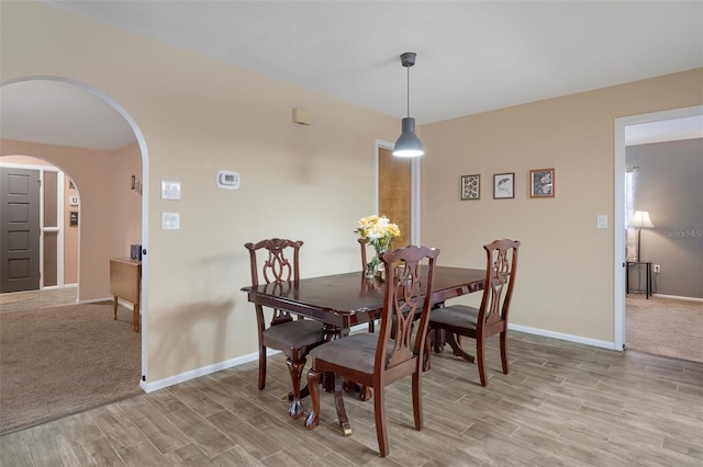 dining space with arched walkways, baseboards, and light wood-style floors
