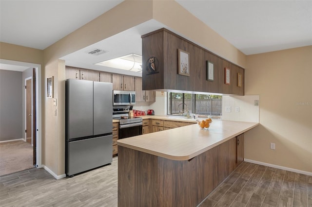 kitchen featuring light wood-type flooring, stainless steel appliances, light countertops, a peninsula, and visible vents