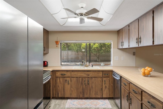 kitchen featuring a sink, light wood-type flooring, backsplash, light countertops, and appliances with stainless steel finishes