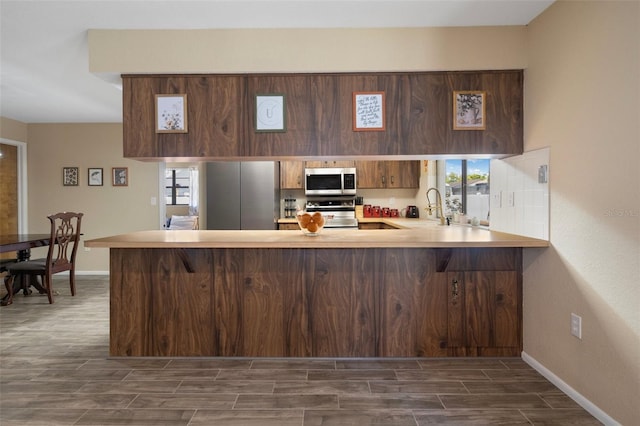 kitchen featuring a peninsula, a sink, baseboards, light countertops, and appliances with stainless steel finishes