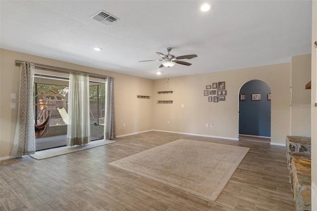 unfurnished room with a ceiling fan, wood finished floors, arched walkways, baseboards, and visible vents