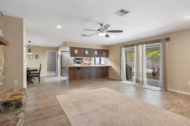 kitchen with light wood-type flooring, a peninsula, visible vents, and appliances with stainless steel finishes