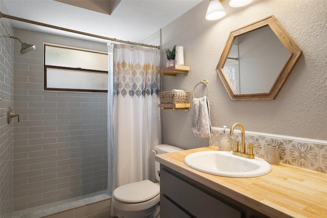 bathroom with a textured wall, a tile shower, vanity, and toilet