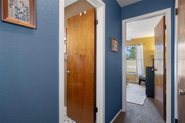 hall featuring baseboards, arched walkways, a textured wall, and carpet