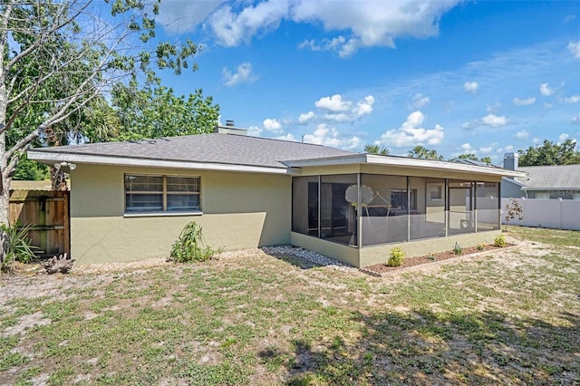 back of property featuring fence, a yard, roof with shingles, stucco siding, and a sunroom