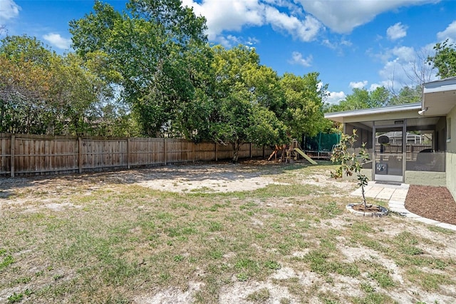 view of yard with a fenced backyard, a sunroom, and a playground