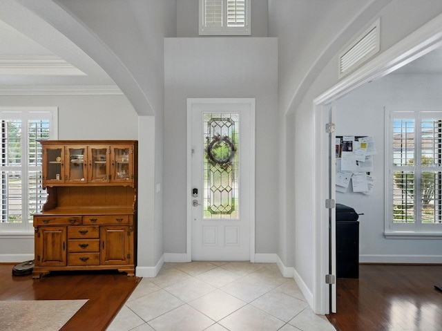 foyer featuring visible vents, arched walkways, light wood-style floors, and crown molding