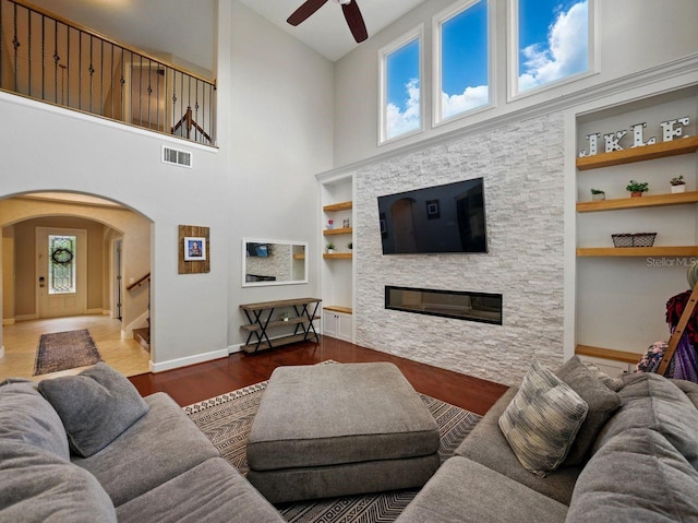 living room featuring ceiling fan, a stone fireplace, visible vents, built in features, and arched walkways