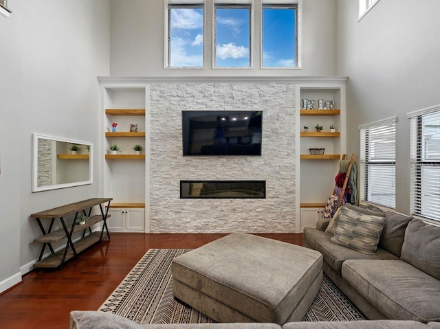 living area with built in features, a towering ceiling, a stone fireplace, and wood finished floors