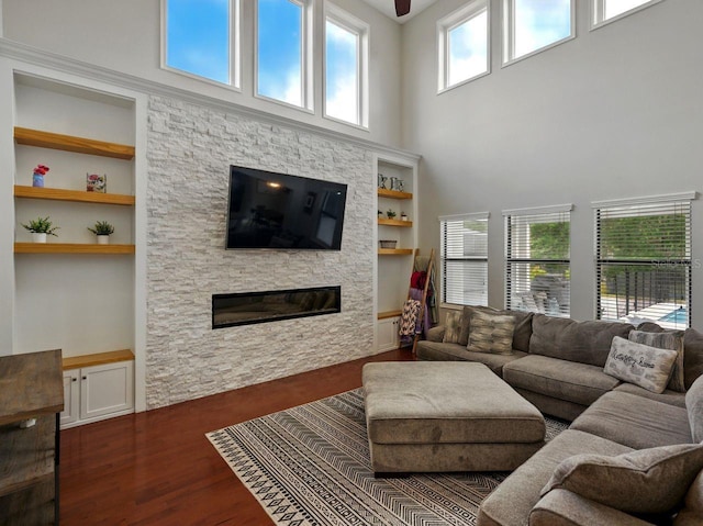 living area featuring built in features, a stone fireplace, wood finished floors, and a towering ceiling