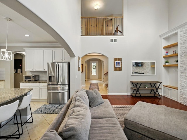 living area featuring arched walkways, built in shelves, a towering ceiling, visible vents, and ornamental molding