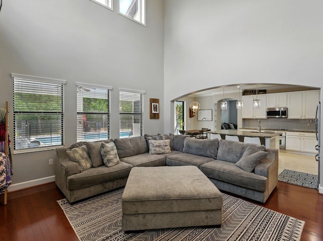 living room with arched walkways, light wood finished floors, a towering ceiling, and a wealth of natural light