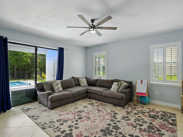living area featuring baseboards, a ceiling fan, tile patterned floors, and a healthy amount of sunlight