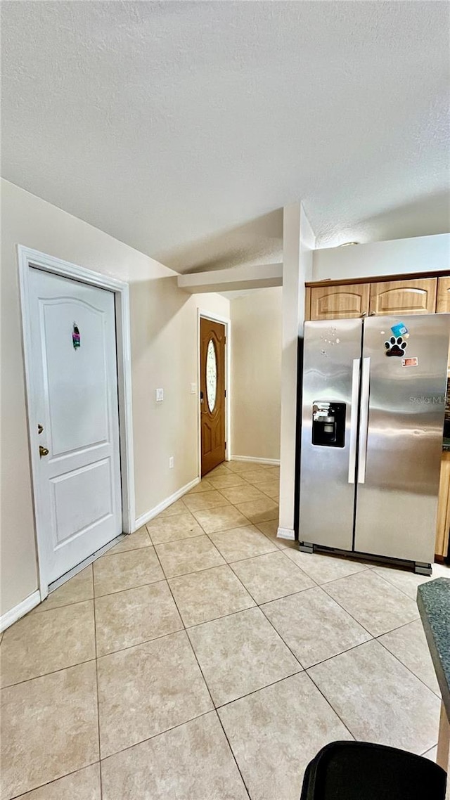 interior space featuring stainless steel fridge with ice dispenser, light tile patterned floors, and a textured ceiling