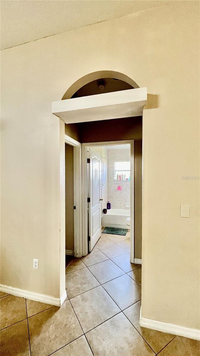 corridor featuring baseboards, light tile patterned flooring, and arched walkways