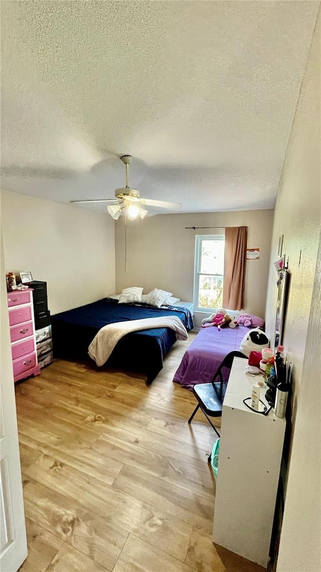 bedroom featuring a ceiling fan, light wood-style flooring, and a textured ceiling