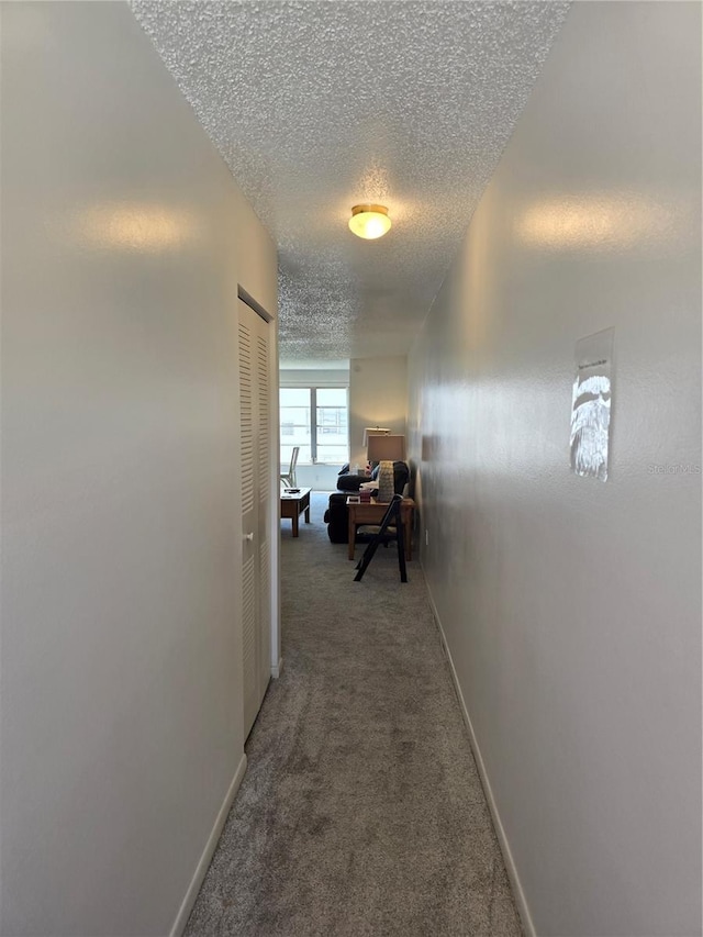 hall with baseboards, light carpet, and a textured ceiling