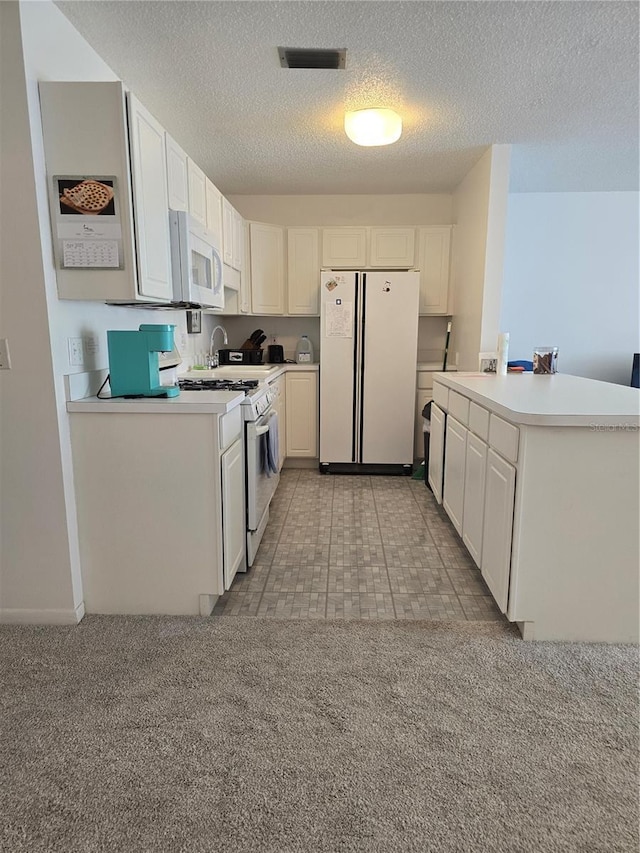 kitchen featuring a textured ceiling, light countertops, white appliances, and visible vents