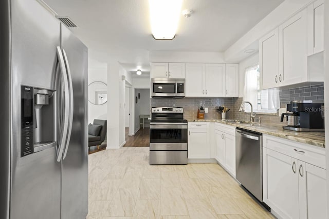 3600 46th St N, Saint Petersburg, FL 33713 - kitchen featuring white cabinets, appliances with stainless steel finishes, light stone counters, a sink, and backsplash