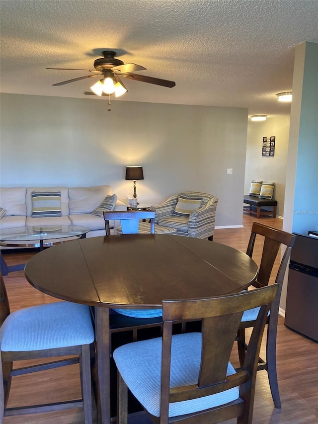 dining room with a ceiling fan, a textured ceiling, wood finished floors, and baseboards
