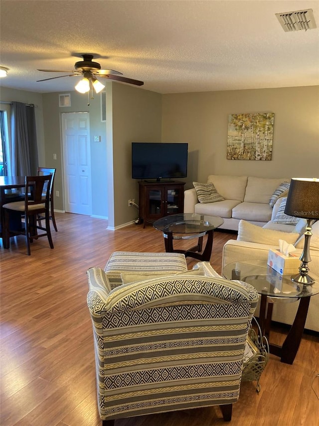 living area with wood finished floors, a ceiling fan, a textured ceiling, and baseboards