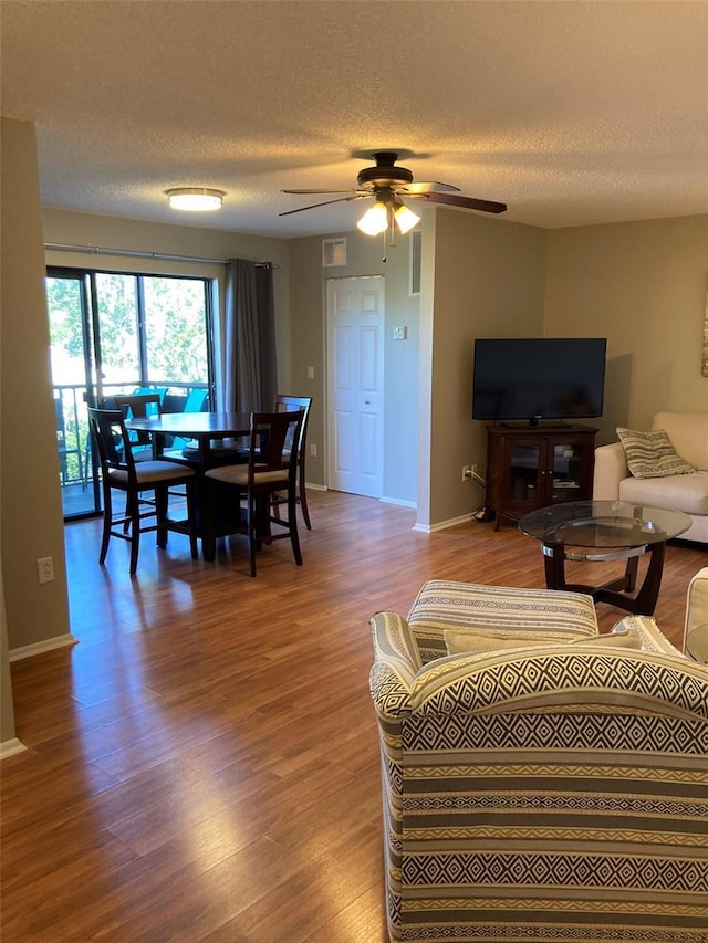 living room with wood finished floors, ceiling fan, a textured ceiling, and baseboards