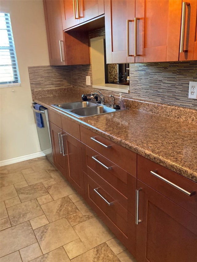 kitchen with a sink, baseboards, backsplash, dark countertops, and dishwasher