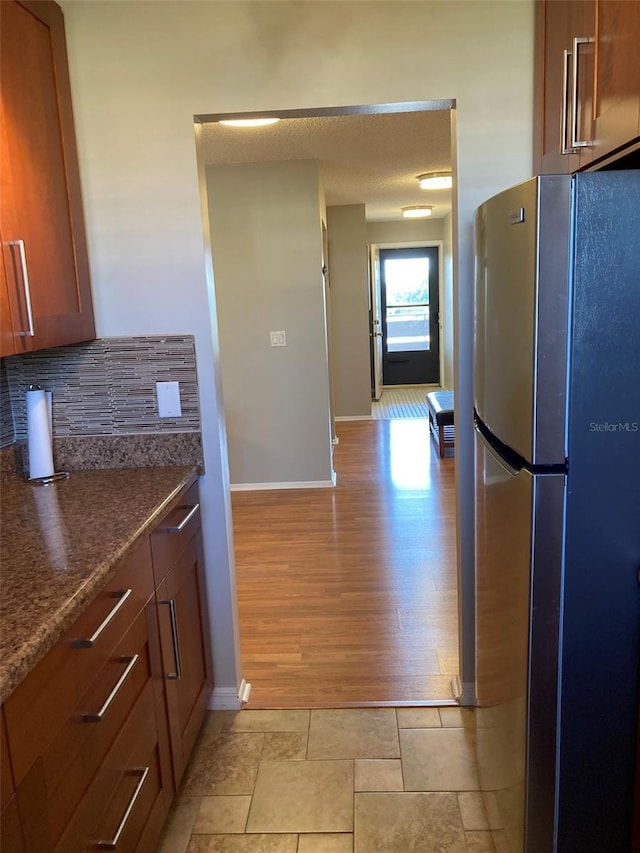 kitchen featuring freestanding refrigerator, baseboards, backsplash, brown cabinetry, and light wood-type flooring