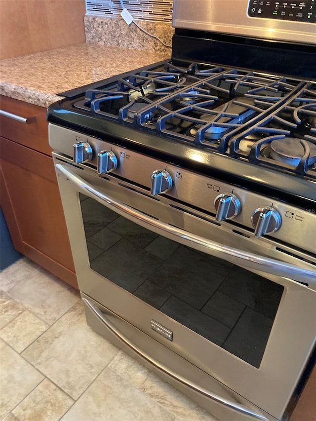 kitchen view of stainless steel gas range oven, decorative backsplash, and light countertops