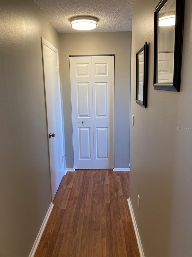 hallway featuring dark wood finished floors, a textured ceiling, and baseboards