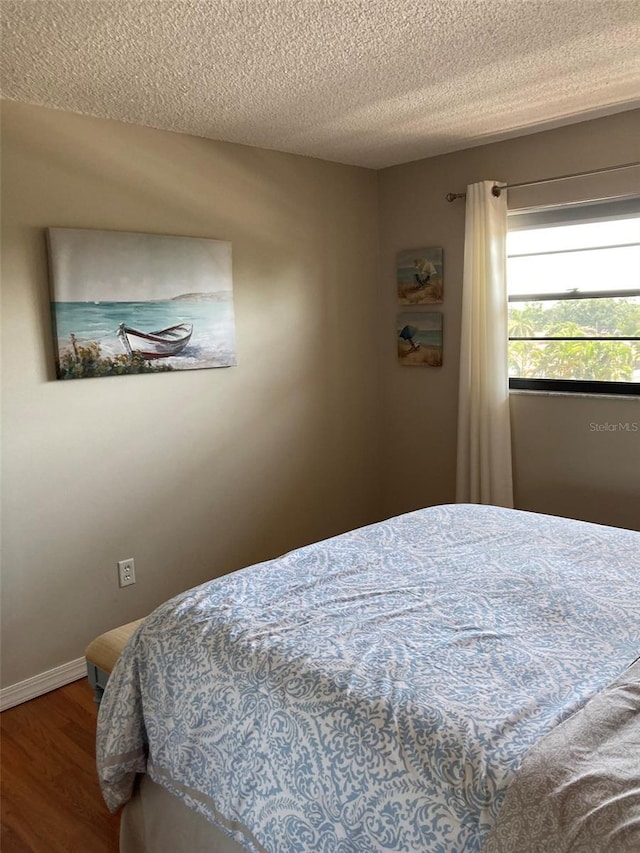 bedroom featuring wood finished floors, a textured ceiling, and baseboards