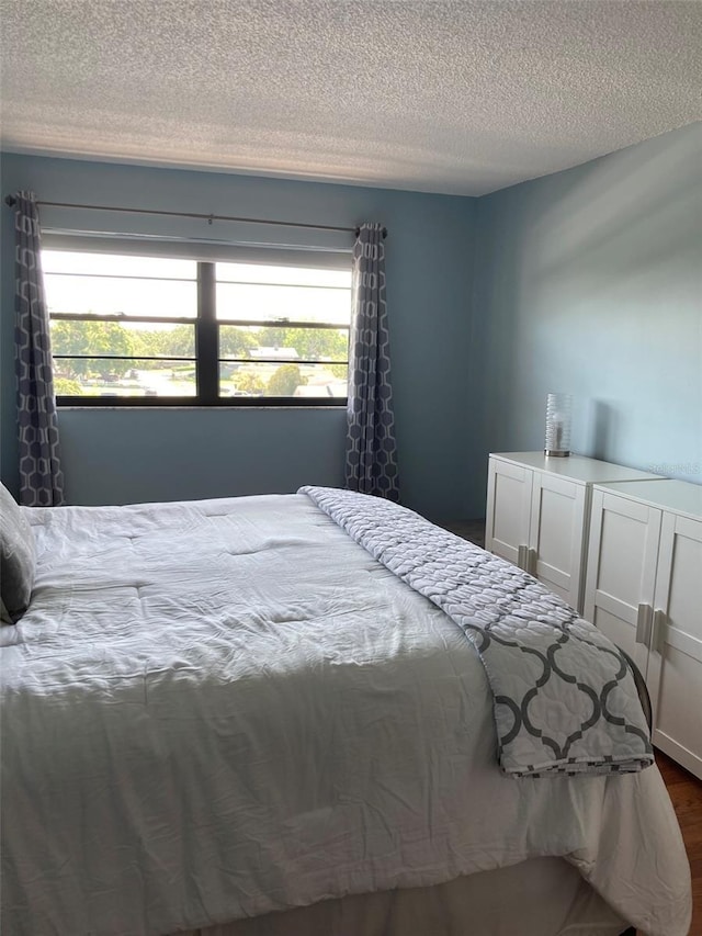 bedroom featuring a textured ceiling, multiple windows, and dark wood-type flooring