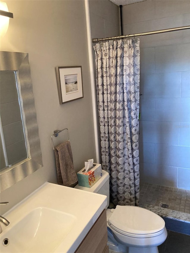 bathroom with a tile shower, toilet, and vanity