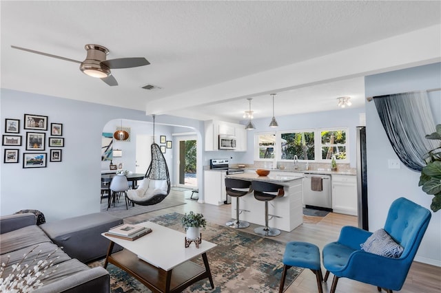 living area featuring a textured ceiling, ceiling fan, arched walkways, light wood finished floors, and visible vents