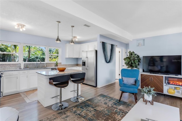 kitchen with light stone countertops, white cabinets, stainless steel fridge, and light wood-style floors