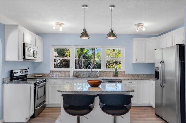 kitchen with white cabinets, appliances with stainless steel finishes, light stone countertops, and a kitchen island