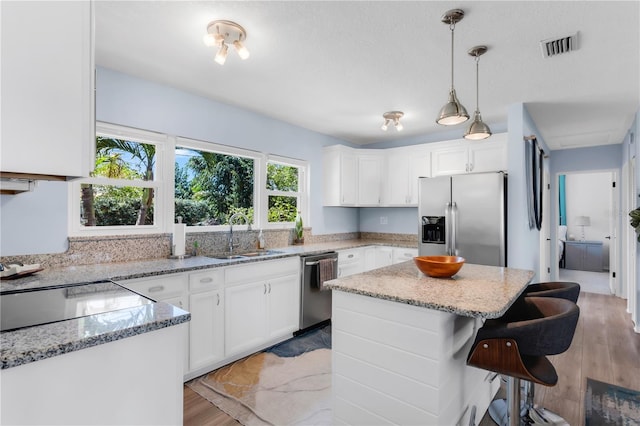 kitchen with light stone counters, a sink, a breakfast bar area, white cabinetry, and appliances with stainless steel finishes