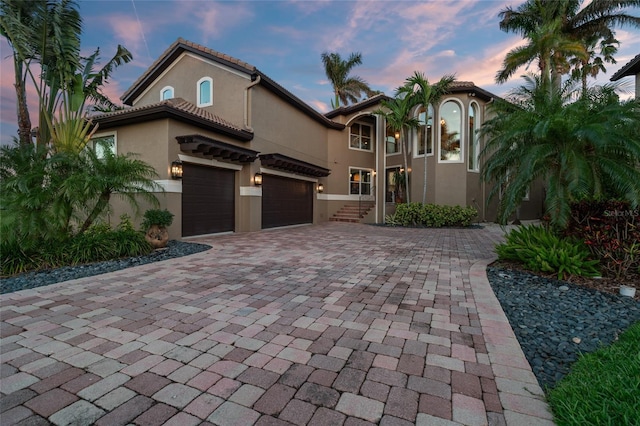 mediterranean / spanish-style home featuring stucco siding, decorative driveway, and a garage