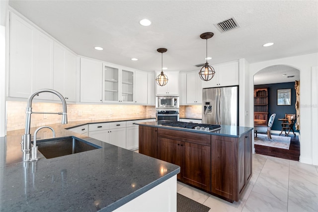 kitchen with a sink, glass insert cabinets, arched walkways, stainless steel appliances, and visible vents