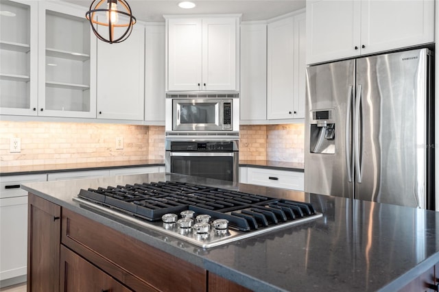 kitchen featuring white cabinets, stainless steel appliances, dark stone counters, and glass insert cabinets