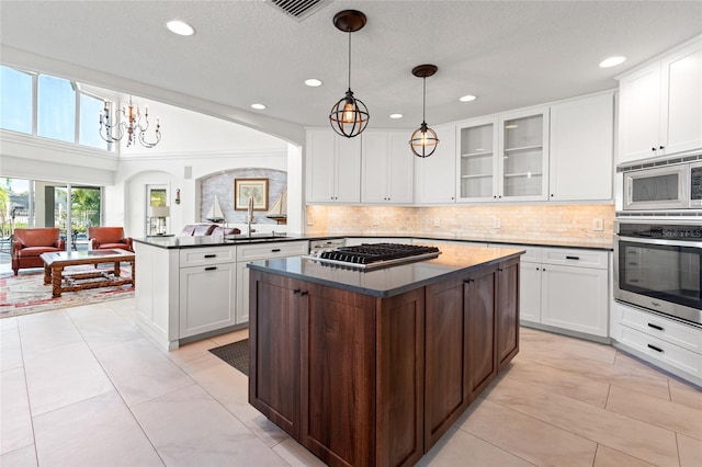 kitchen with stainless steel appliances, a peninsula, a sink, an inviting chandelier, and decorative backsplash